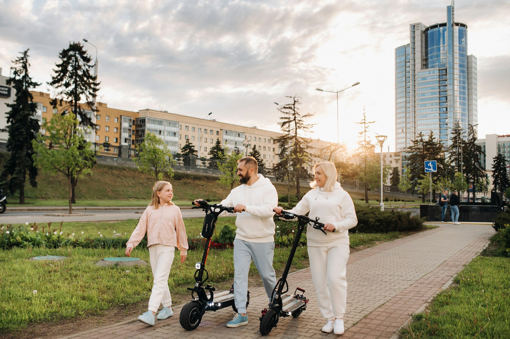 A family in white clothes walks around the city with electric scooters at sunset.Outdoor activities